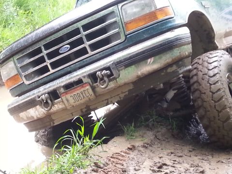 1996 Ford Bronco - A green Ford truck is stuck in the mud, showing its front grille and a large tire.