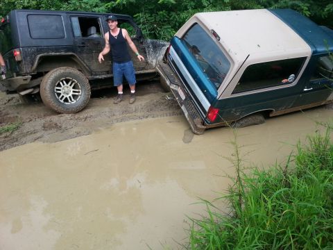 1996 Ford Bronco - Two off-road vehicles, a 1996 Ford Bronco and a Jeep Wrangler, are stuck in a mud pit.