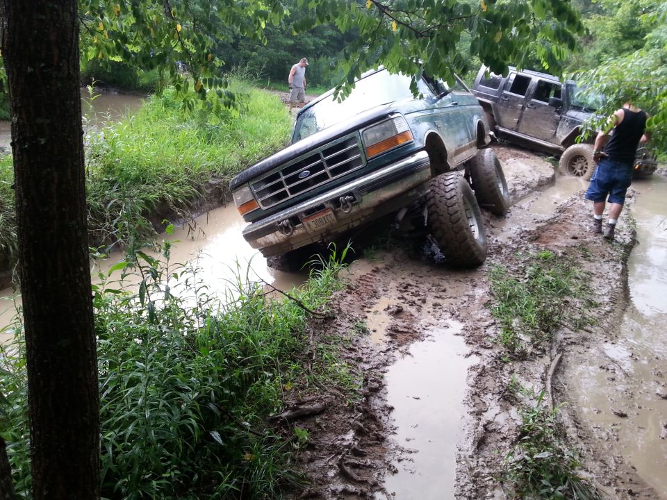 Green Ford F-Series truck stuck in mud with large tires, front grille visible