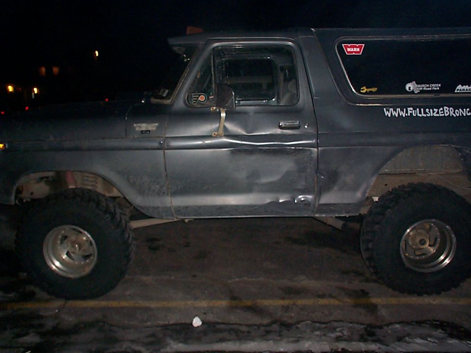 Dark gray 1978 Ford Bronco side view, dented driver's door, off-road tires