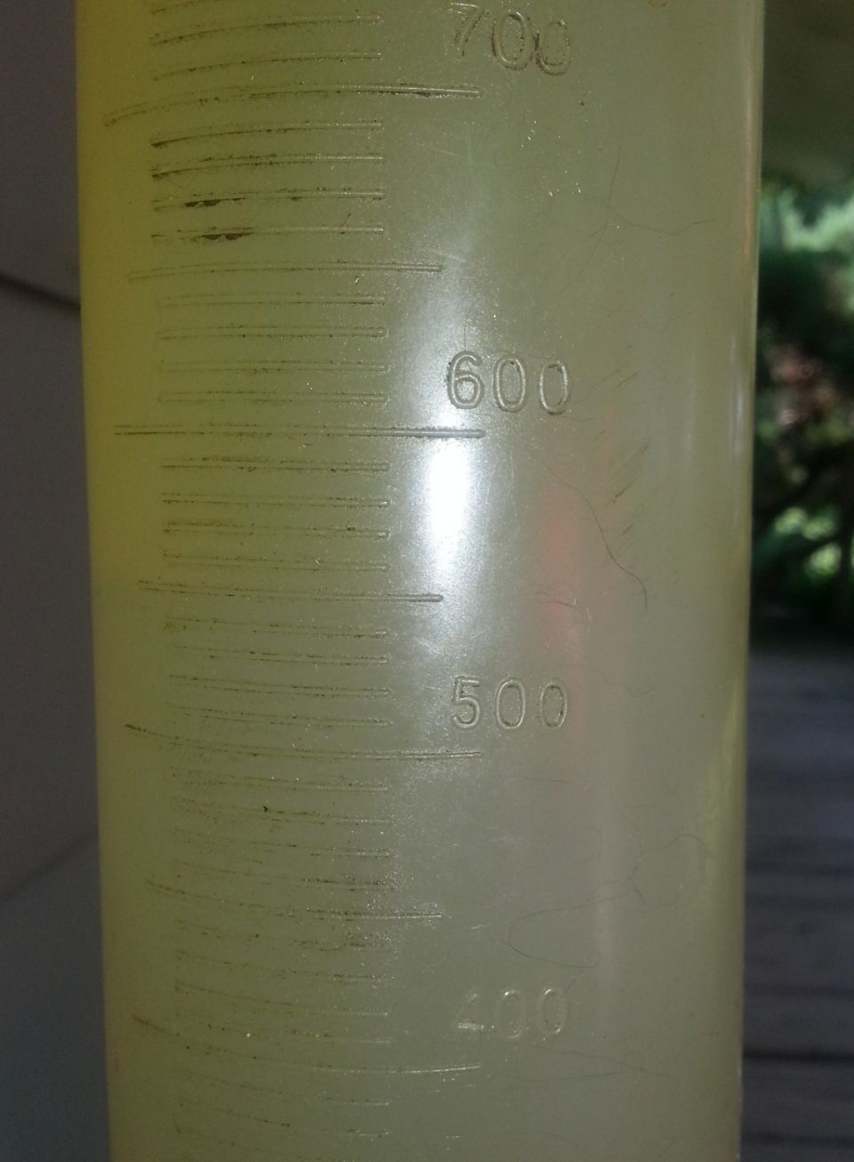 Yellow plastic graduated cylinder with markings for 400, 500, 600, and 700 units. Supermotors.net logo at bottom