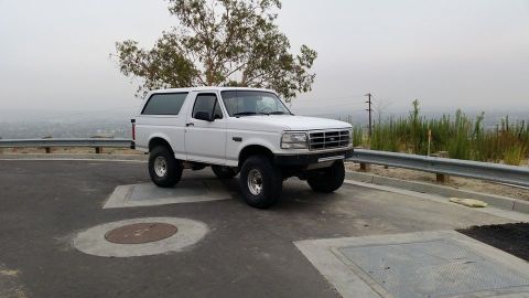 1988 Ford Bronco - White Ford Bronco SUV parked on a paved area with a distant city view.