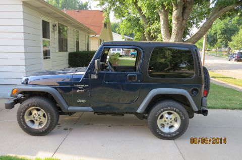 2000 Jeep Wrangler - A dark blue Jeep Wrangler is parked on a driveway next to a house.
