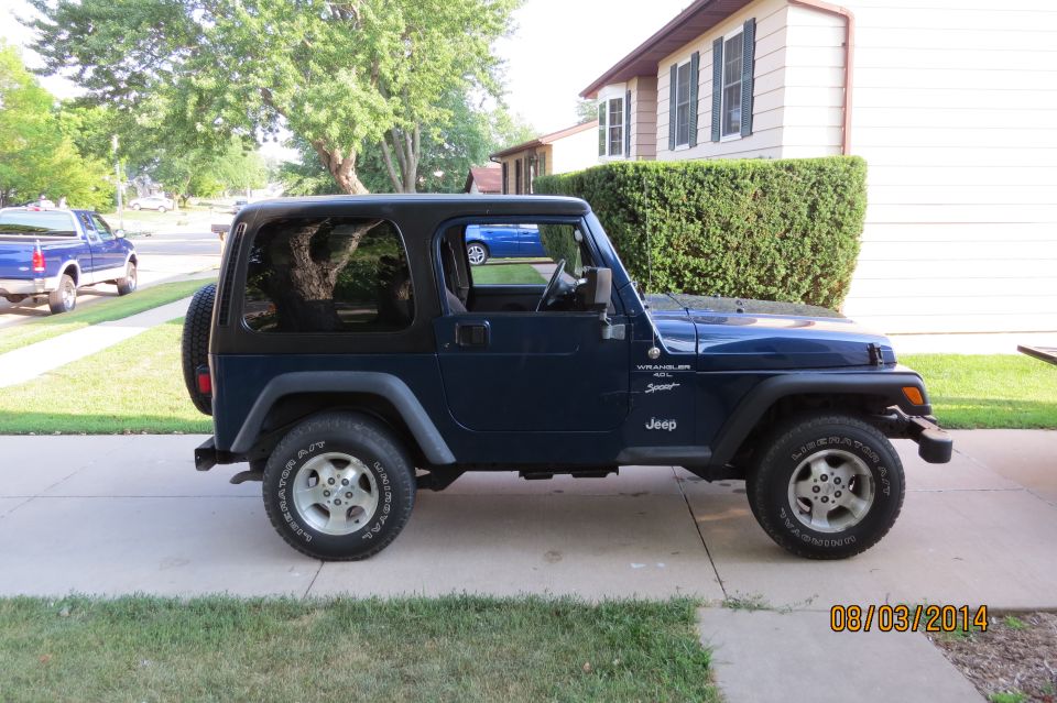Blue Jeep Wrangler parked in driveway. It has a black hardtop and spare tire on the back