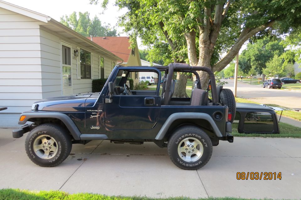 Dark blue Jeep Wrangler parked on driveway, soft top removed and leaning against the vehicle. Date stamp 08/03/2014