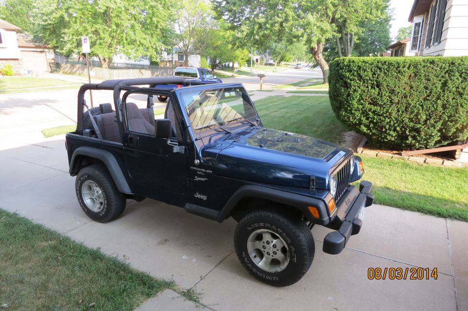 Dark blue Jeep Wrangler parked on a driveway, soft top removed, showing interior and front grille