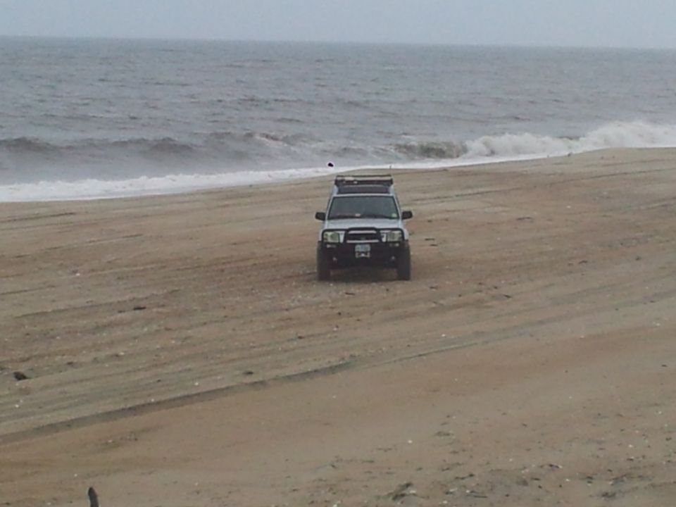 White SUV with a roof rack parked on a sandy beach near the ocean