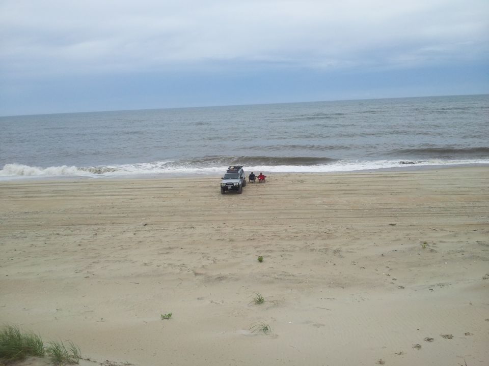 Silver SUV on beach with two people in chairs