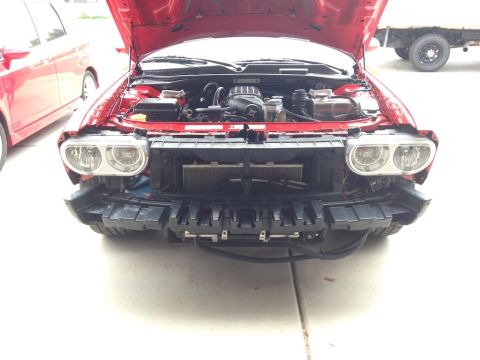 2010 Dodge Challenger - The front of a red Dodge Challenger is shown with its hood up and bumper removed, revealing the engine and radiator.