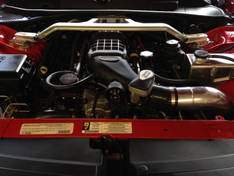 2010 Dodge Challenger - Engine bay view shows a supercharger and intake system, with visible warning labels on the red fender.