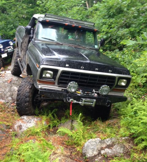 1979 Ford Bronco - This modified Ford Bronco is navigating a rocky trail with dense foliage surrounding it.