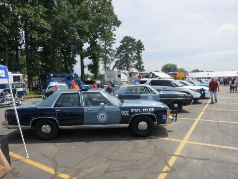 1991 Ford LTD Crown Victoria - two-tone blue Massachusetts State Police sedan marked 90E lines up beside other cruisers at a sunny outdoor emergency-vehicle show.