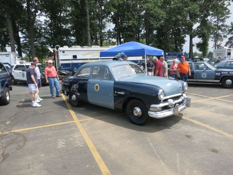 1991 Ford LTD Crown Victoria - restored 1950s-era two-tone blue police sedan with chrome bumpers sits on display as spectators look on at an outdoor show.