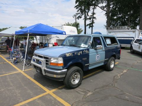 1991 Ford LTD Crown Victoria - two-tone blue State Police Ford Bronco SUV with a front brush guard and roof light sits beside a pop-up tent at a vehicle show.