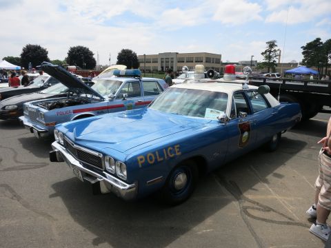 1991 Ford LTD Crown Victoria - blue vintage four-door sedan lettered POLICE with rooftop emergency lights is displayed among other cruisers at a show.