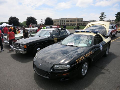 1991 Ford LTD Crown Victoria - black-and-tan Chevrolet Camaro marked STATE TROOPER sits with hood open beside other police cars at an outdoor show.