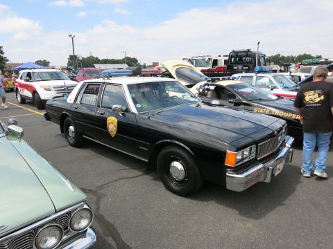 1991 Ford LTD Crown Victoria - black-and-white State Trooper sedan with chrome bumpers and roof lights is parked among other cruisers at an outdoor event.