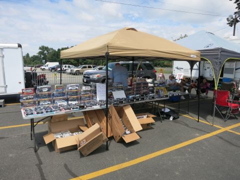 1991 Ford LTD Crown Victoria - tan pop-up tent shelters folding tables displaying boxed diecast model cars with cardboard boxes stacked underneath.