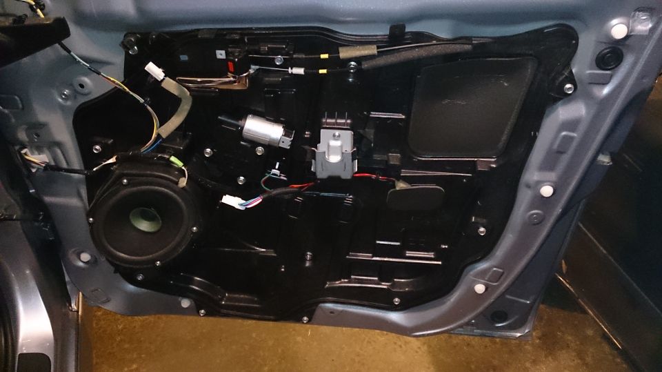 Car door interior panel removed, showing speaker, window motor, and wiring harness. Blue exterior paint visible