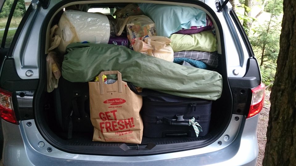 Silver car's open trunk packed with suitcases, sleeping bags, pillows, and grocery bags