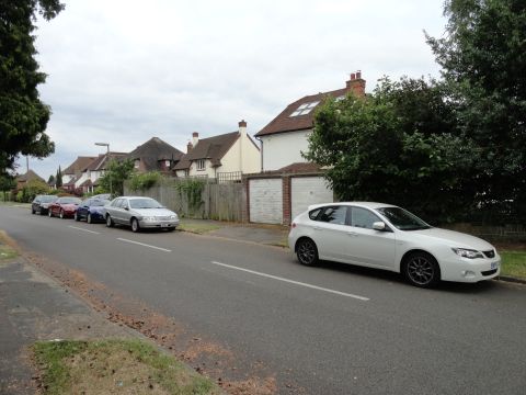 1999 Ford Fairlane - A white Subaru Impreza hatchback is parked on the right side of a street, with several other cars lined up on the left.