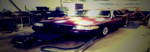 2004 Ford Crown Victoria - A maroon 2004 Ford Crown Victoria is positioned on a dynamometer in a workshop setting.
