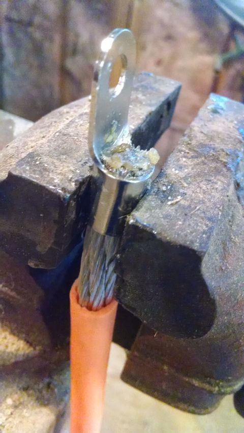 1995 Ford Bronco - Close-up of a battery cable terminal secured in a vise, showing the wire strands and orange insulation. The website SUPERMOTORS.NET is visi…