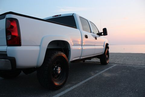 2006 Chevrolet Silverado 2500 - White pickup truck parked on pavement near the ocean at sunset.