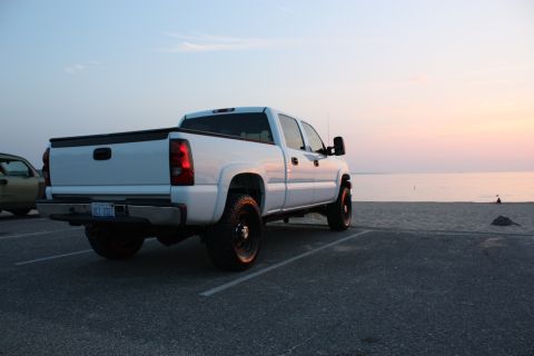 2006 Chevrolet Silverado 2500 - A white pickup truck is parked in a lot by the beach during a sunset.