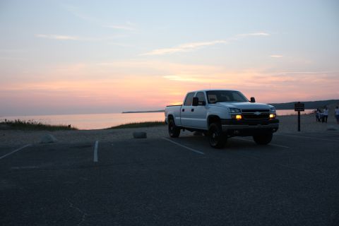 2006 Chevrolet Silverado 2500 - A white pickup truck is parked in a lot overlooking the water as the sun sets.