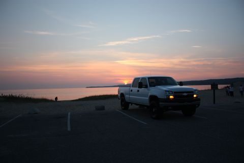 2006 Chevrolet Silverado 2500 - A white Chevrolet Silverado pickup truck is parked near a beach as the sun sets over the water.