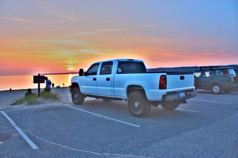 2006 Chevrolet Silverado 2500 - A white 2006 Chevrolet Silverado 2500 is parked near the beach as the sun sets over the water.