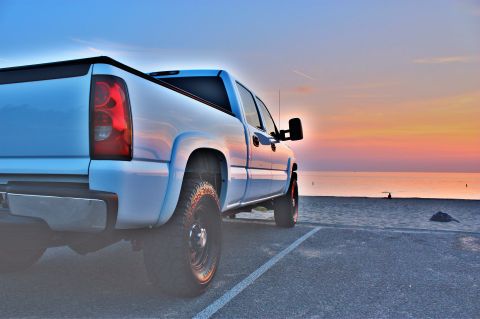 2006 Chevrolet Silverado 2500 - A white pickup truck is parked on a paved area next to a sandy beach during a colorful sunset.