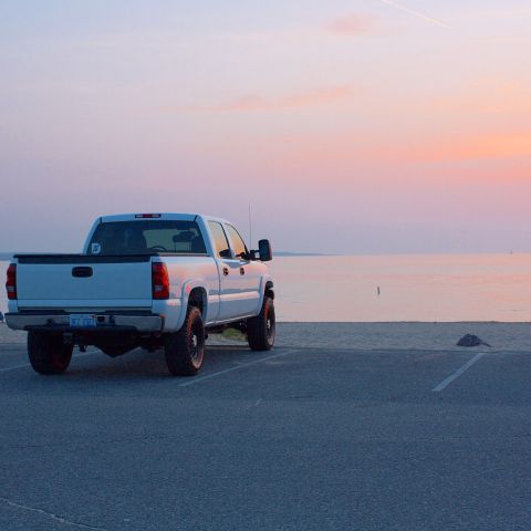 2006 Chevrolet Silverado 2500 - A white pickup truck is parked near the water's edge during a colorful sunset.