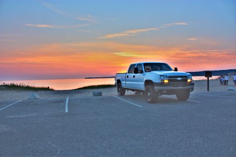 2006 Chevrolet Silverado 2500 - A white pickup truck is parked in a lot by the water as the sun sets over the horizon.
