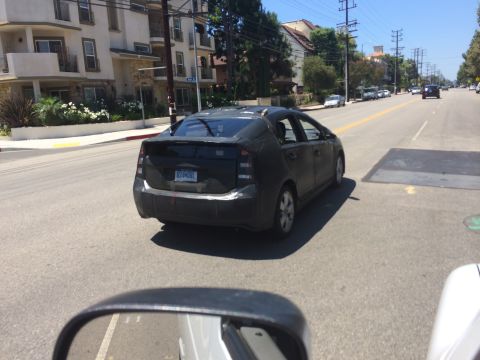 1968 Ford Mustang - A black Toyota Prius, partially covered in camouflage wrap, is seen from behind on a city street. The license plate is visible.