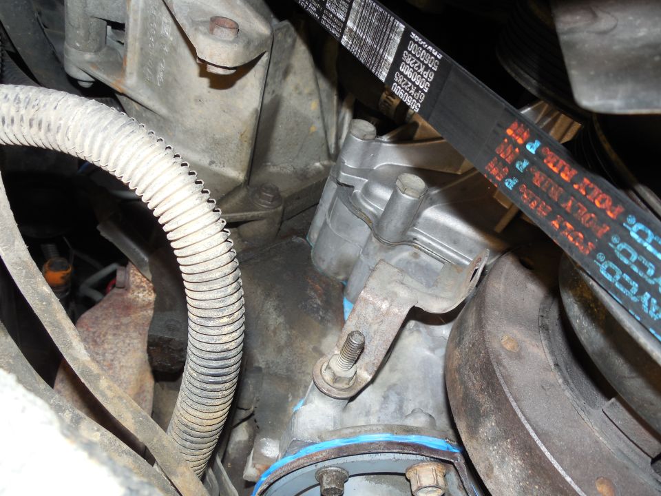 Close-up of an engine component with a serpentine belt and part numbers visible