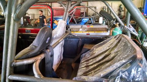 1985 Jeep CJ7 - Modified vehicle interior with roll cage and custom seats, showing multiple vehicles in a workshop setting.