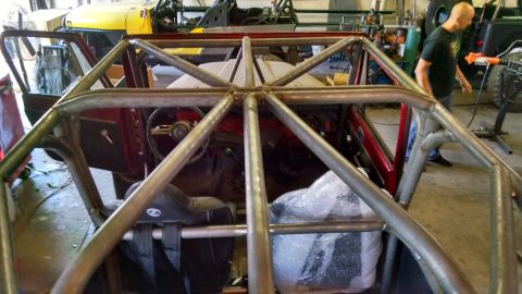 1985 Jeep CJ7 - A custom roll cage is being installed inside a red Jeep, with another Jeep visible in the workshop.