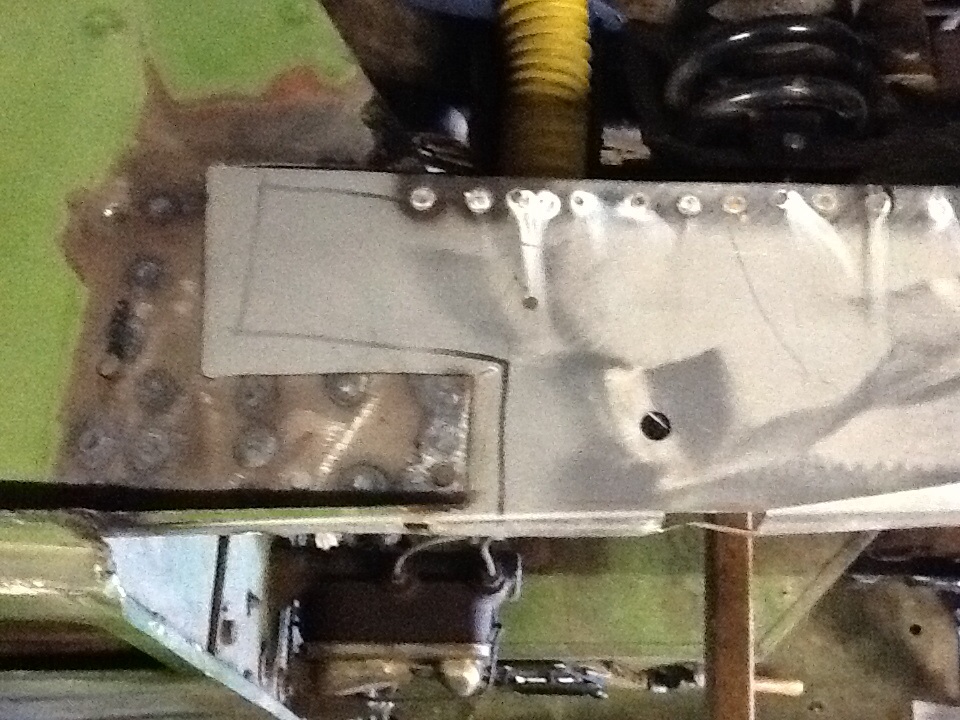 Close-up of metal panel repair on a vehicle frame, showing welds and cut lines
