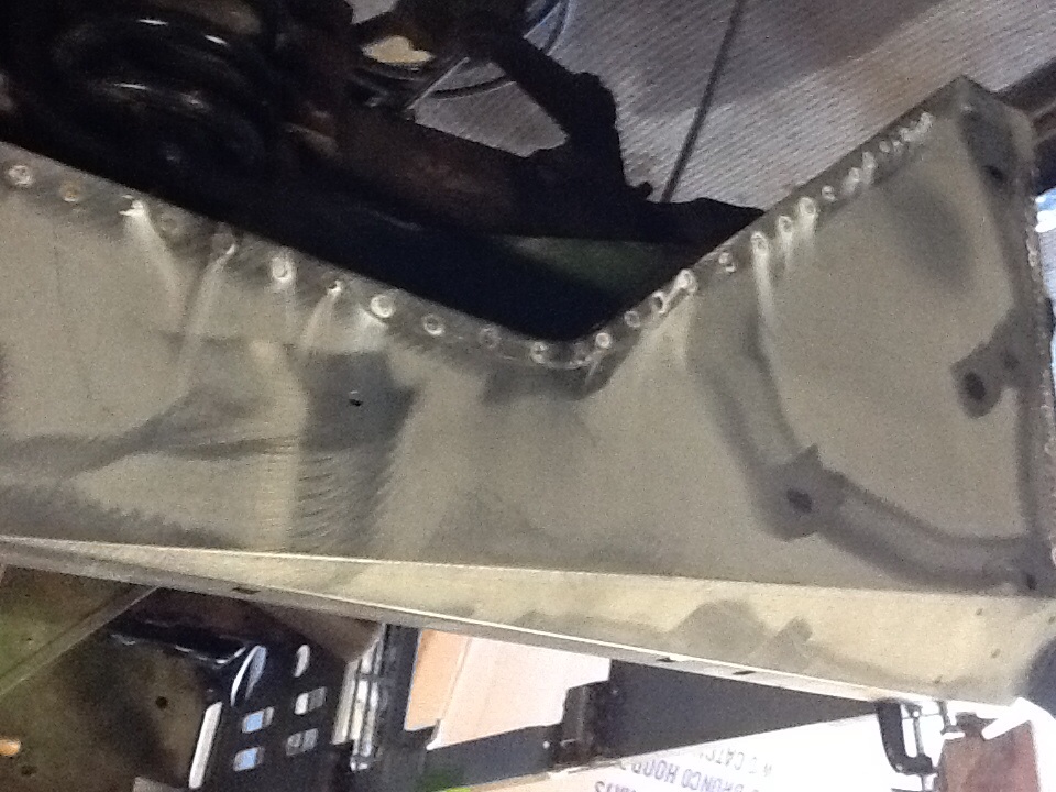 Close-up of a riveted metal panel, possibly a repair or custom part, with suspension components visible above