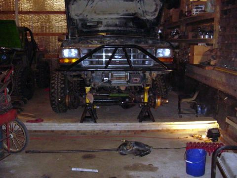 1992 Ford Bronco - Front end of a 1992 Ford Bronco undergoing work, with the hood up and the vehicle supported by jack stands.