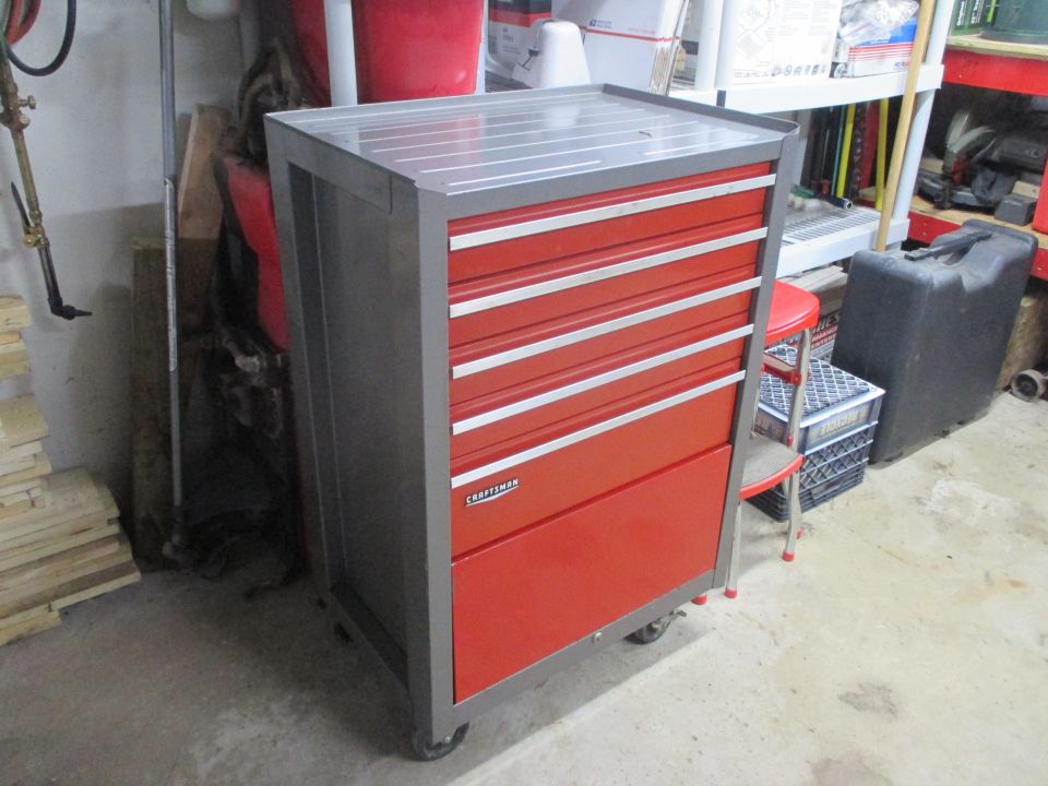 Red and gray Craftsman tool chest with multiple drawers and silver trim. A small red stool is next to it
