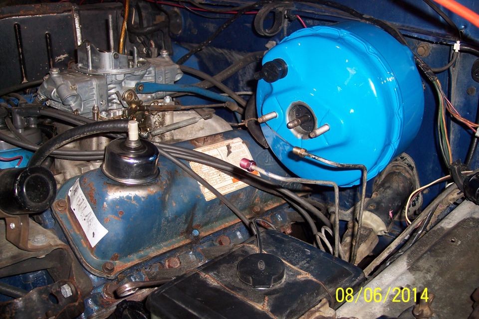 Engine bay of a 1978 Ford Bronco with a blue brake booster and carburetor