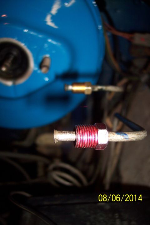 1978 Ford Bronco - Close-up of a red brake line fitting connected to a metal tube, with a blurred blue component in the background.