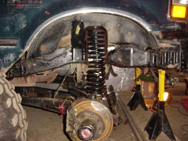 Green 1992 Ford Bronco front wheel well and suspension during repair, with large off-road tire visible