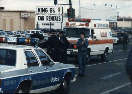 1991 Ford LTD Crown Victoria - A police car and an ambulance are parked on a street, with "KING B's CAR RENTALS" visible in the background.