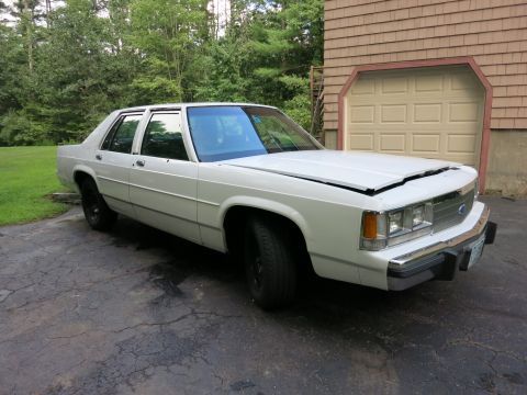 1991 Ford LTD Crown Victoria - A white 1991 Ford Crown Victoria is parked on a cracked driveway in front of a beige garage door.