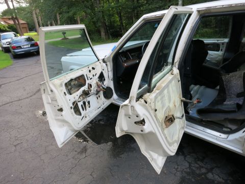 1991 Ford LTD Crown Victoria - The interior of a white Ford Crown Victoria is exposed with both front doors removed, revealing the inner workings and wiring.