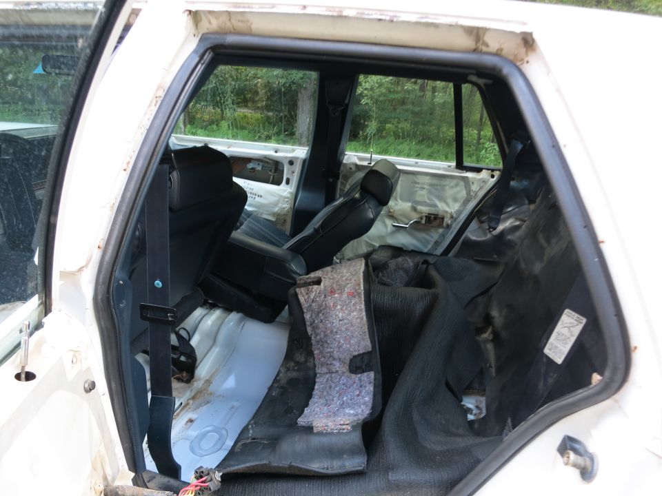 White car interior with torn upholstery and exposed metal, showing front seats and rear door panels